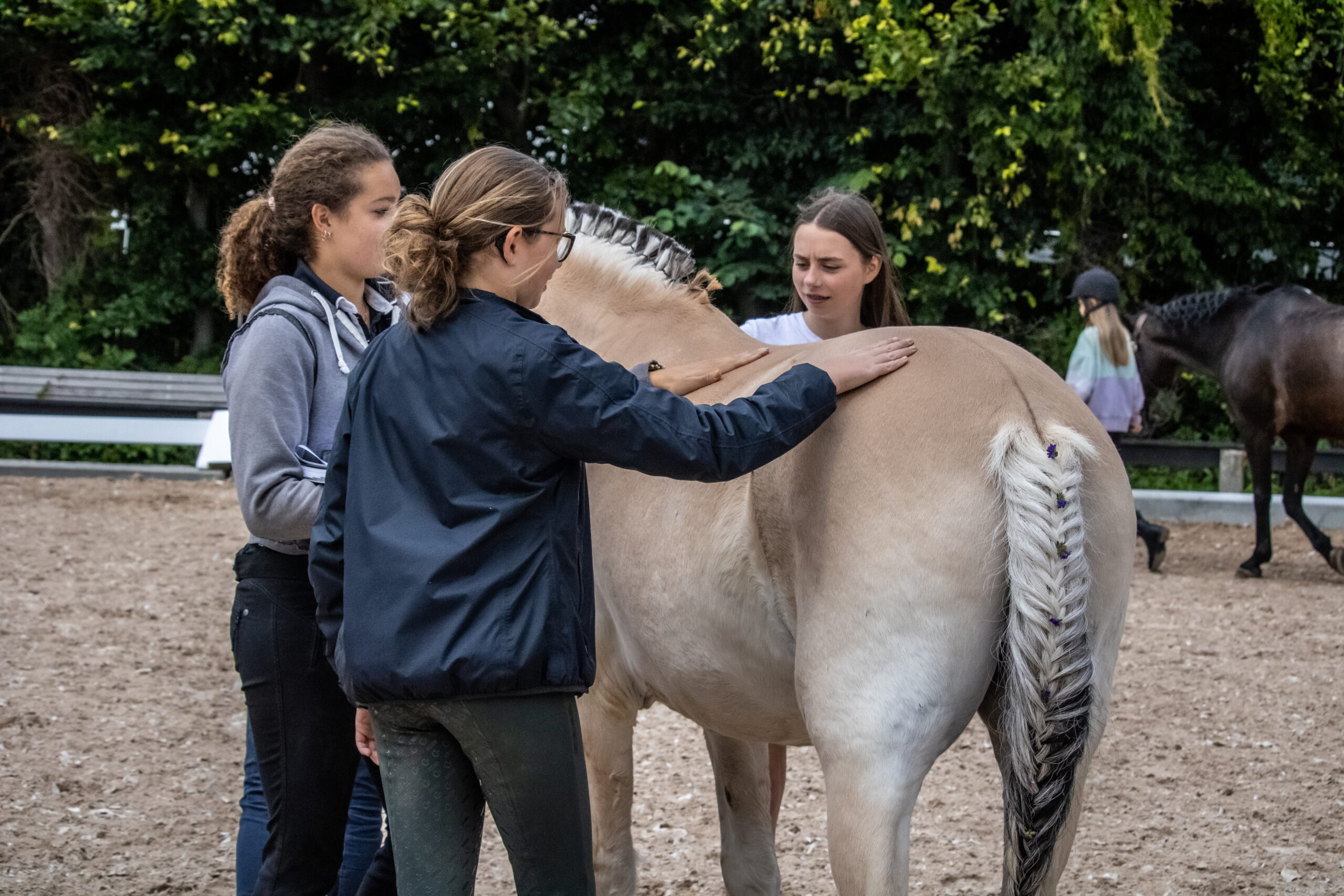 Tre unge ryttere arbejder roligt med en pony på ridebanen